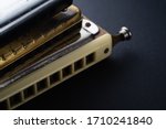 Small photo of the old two diatonic and one chromatic harmonica, one on top of the other on a dark background. Horizontal orientation.