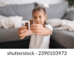Small photo of Little crafty girl eats sweets at home. Kid eating chocolate and have fun. Chaos at home. Focus on hands