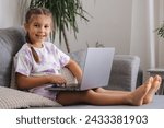 Small photo of Happy and smart little girl using laptop at home. Five year old girl try to use smart devise