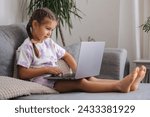 Small photo of Happy and smart little girl using laptop at home. Five year old girl try to use smart devise