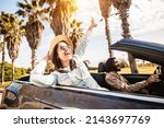 Happy young couple having enjoying summer vacation on convertible car - Man and woman laughing while driving a cabriolet auto outdoors - Travel and holidays concept - Soft focus on woman face