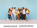 Happy multiracial students standing over isolated blue background. Diverse teenage friends having fun talking leaning on campus building college wall