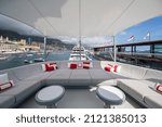 The front deck of huge yacht in port of Monaco at sunny day, landmarks of Monte-Carlo and a lot of motorboats are on background, the lounge zone for a chilling, megayacht is moored in marina