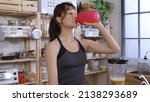 Small photo of waist up sportive asian female taking a gulp of her homemade fruit smoothie after morning exercise. confident yoga instructor holding tumbler.