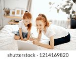 Small photo of Young woman with ginger pony tail using laptop to show her little preschool daughter the educational film about life evolution process, while mother and her female kid spending time together at home