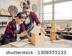 Carpenter building a wooden birdhouse together with his kid. A little son is participating actively in hand made process. Happy fatherhood and DIY concept.