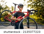 Cyclo-cross competition member Man biker carrying bike up on going on road,Professional road bicycle racer. Strong athletic man in sportswear and protective helmet training in forest at sunset