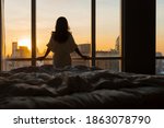 Beautiful asian woman is waking up in the morning, Sun shines on her from the big window. Happy young girl greets new day with warm sunlight flare and city scenery in the window. Co
