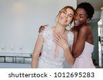Gorgeous bride in wedding gown having fun with bridesmaid in hotel room. Cheerful bride and bridesmaid on the wedding day.