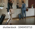 Woman carrying suitcase and talking on mobile phone in a hotel lobby. Traveler female walking with her luggage in hotel hallway.