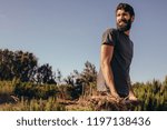 Small photo of Portrait of happy young beard man throwing loose hay and straw from the farm wroth pitch fork. Male farmer working in the farm with pitch fork.