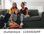 Small photo of Three young girls sitting together at home watching television and laughing. Teenage girls at a sleepover having fun watching TV sitting in the living room.