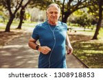Cheerful senior man jogging in park listening to music on earphones. Senior fitness person running in park for good health.