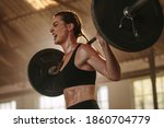 Female bodybuilder doing exercise with heavy weight bar. Fitness woman sweating from squats workout at gym. Female putting effort and screaming while exercising with heavy weights.