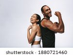 Smiling fitness couple standing back to back against white background. Fit couple showing arm muscles standing together.