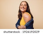 Portrait of a female smiling after getting a vaccine. Woman holding down her shirt sleeve and showing her arm with bandage after receiving vaccination.