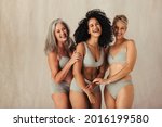 Happy women of different ages embracing their natural bodies. Group of body positive women wearing underwear and standing together. Women posing against a studio background