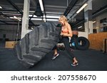 Muscular young woman flipping tire at gym. Fit female athlete performing a tire flip at crossfit gym.