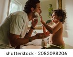 Small photo of Curious young boy applying shaving foam on his father's face. Caring young boy helping his father shave his facial hair in the bathroom. Loving father and son bonding at home.