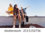 Small photo of Energetic female friends enjoying themselves outdoors. Three happy friends smiling while hanging out on a wall in the city. Cheerful female youngsters having fun together.