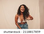 Feeling cheerful in the studio. Happy young woman laughing while standing against a studio background. Body positive young woman feeling comfortable in denim jeans and a bra.