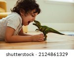 Small photo of Adventurous young boy imitating a dinosaur toy while lying on the floor in his play area. Creative little boy having fun during playtime at home.