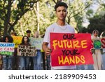 Teenage boy looking at the camera while leading a march against climate change. Group of multicultural youth activists protesting against global warming. Teenagers joining the global climate strike.