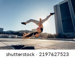 Small photo of Young sportswoman performing a front flip outdoors in city. Female athlete practicing tricking against an urban background.