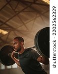 Small photo of Fitness man doing back squats workout with heavy weight barbell. Sportsman doing exercise with heavy weights at old warehouse.