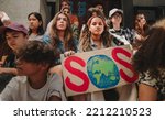 Small photo of Save our planet campaign. Group of multicultural climate activists sitting with posters outside a building. Youth demonstrators protesting against global warming and climate change.
