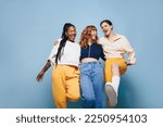 Small photo of Group of cheerful female friends having fun while embracing each other. Three happy young women laughing and having a good time while standing against a studio background.