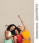 Small photo of Three young women laughing happily as they stand together in a studio wearing sports clothing. Group of female friends celebrating their fit, healthy and sporty lifestyle.
