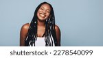 Small photo of Portrait of an African woman with dreadlocks and body piercings smiling at the camera. Happy young woman feeling confident in her style. Fashionable woman standing against a studio background.