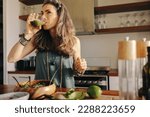 Small photo of Vegan woman drinking some green juice while having a buddha bowl. Mature woman serving herself a healthy plant-based meal in her kitchen. Senior woman eating clean at home.