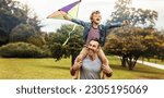 Happy young boy flying a kite while sitting on his father