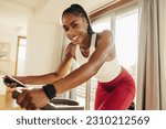 Small photo of Sporty and enthusiastic young woman happily reaching her fitness goals with the help of her home cycling equipment, determined to achieve her fitness objectives and live a healthy lifestyle.
