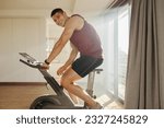 Small photo of Young man enjoys smashing his goals in his indoor cycling workout. Athlete using his high-tech training equipment to get the most out of his home gym and push himself to new heights of fitness.