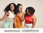 Group of diverse young female athletes are smiling and laughing as they stand together together in the studio dressed in sportswear, celebrating their healthy lifestyle and friendship.