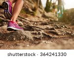 Close up of an athlete's feet wearing sports shoes on a challenging dirt track. Trail running workout on rocky terrain outdoors.