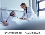 Hospitalized man lying in bed while doctor checking his pulse. Female physician examining male patient in hospital room.