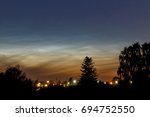 Noctilucent clouds with lower hanging clouds approaching and trees in the foreground