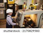 Serious busy female technical engineer standing at cnc lathe and pushing buttons while choosing Cnc machining operations at factory