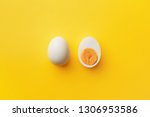 Single whole white egg and halved boiled egg with yolk on a yellow background. Top view