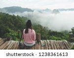 traveller women wear pink sweater and hat sit looking to mist sea with valley and forest view at north of thai land. Travel season backpack concept.