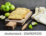 Small photo of Sliced apple and coconut oaf cake on wooden cutting board on dark background