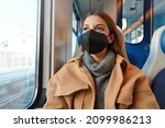 Young thoughtful woman wearing black medical face mask on train looking through the window. Concept of travelling and using public transport during pandemic.