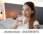Small photo of Beautiful girl in the bed drinks a glass of water just woken up in the morning. Importance of good daily hydration.