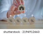 House and property investment and asset management concept. Interest rates, loan mortgage, house tax. Hand holding house icon on wooden circle from percent icon on wooden circle and rise of arrow.