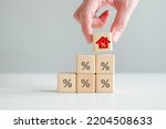 House and property investment and asset management concept. Interest rates, loan mortgage, house tax. Hand holding house icon with percent sign from stack of blocks with percentage icon