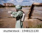 Small photo of A male environmentalist in a protective suit and gas mask takes a sample of water. Scientist doing toxicological study.